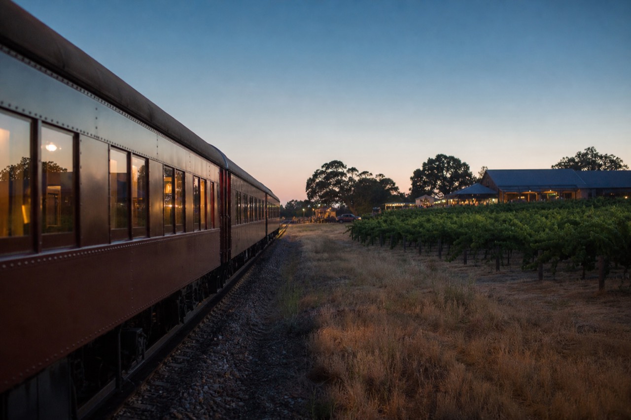 A vintage rail carriage moving along tracks beside a vineyard under a clear sky, warm light, no text, no logos, no people