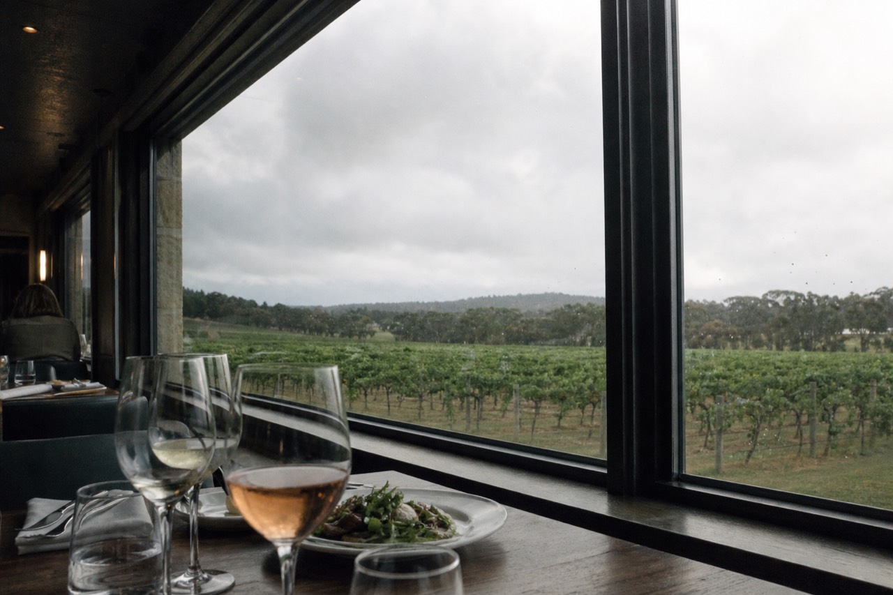 Table set with wine glasses and a plated course beside a large train window looking out on vineyards, warm interior light, no text, no logos, no faces