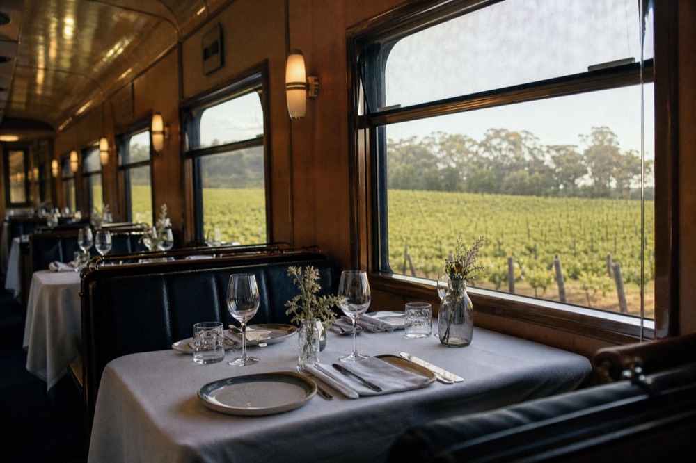 Interior of a dining rail car with tables set for a meal and vineyards through the windows, soft daylight, no text, no logos, no people