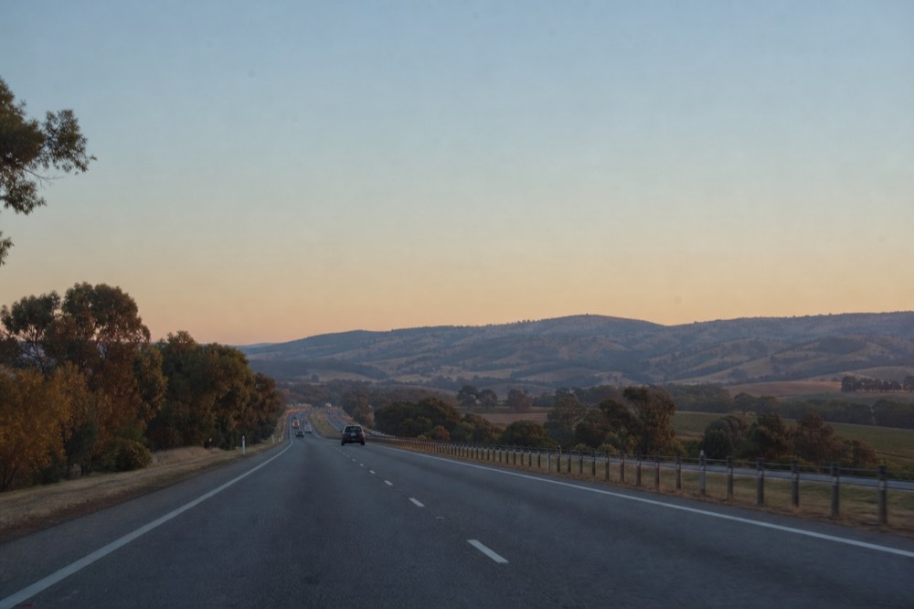 An early-morning freeway heading toward distant green hills with light traffic, soft sunrise light, no text, no logos, no people