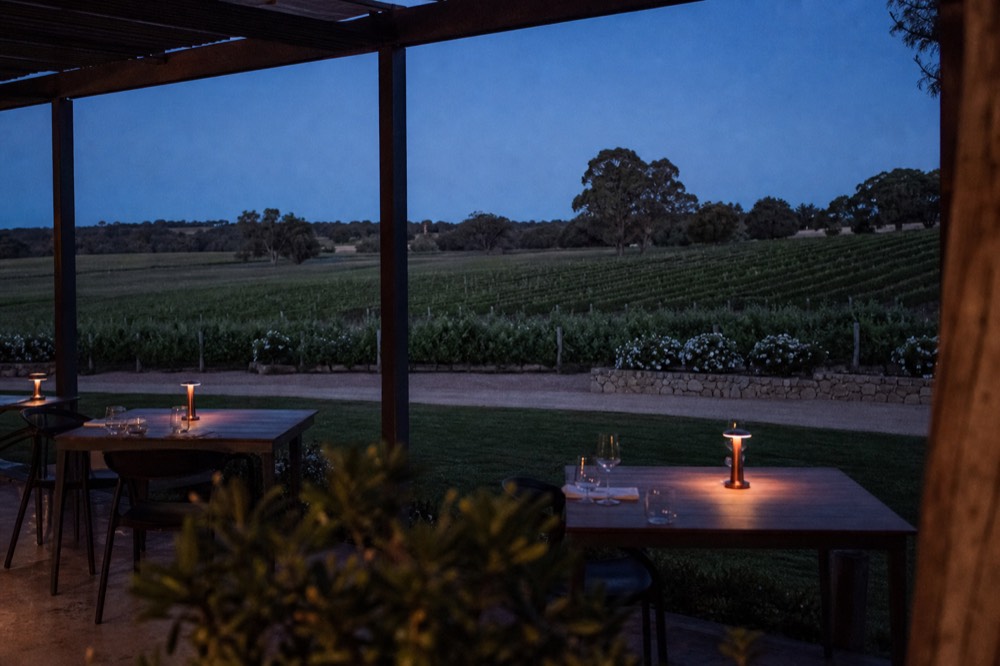 A quiet reserved tasting terrace overlooking vineyard rows with a few set tables, warm afternoon light, no text, no logos, no people